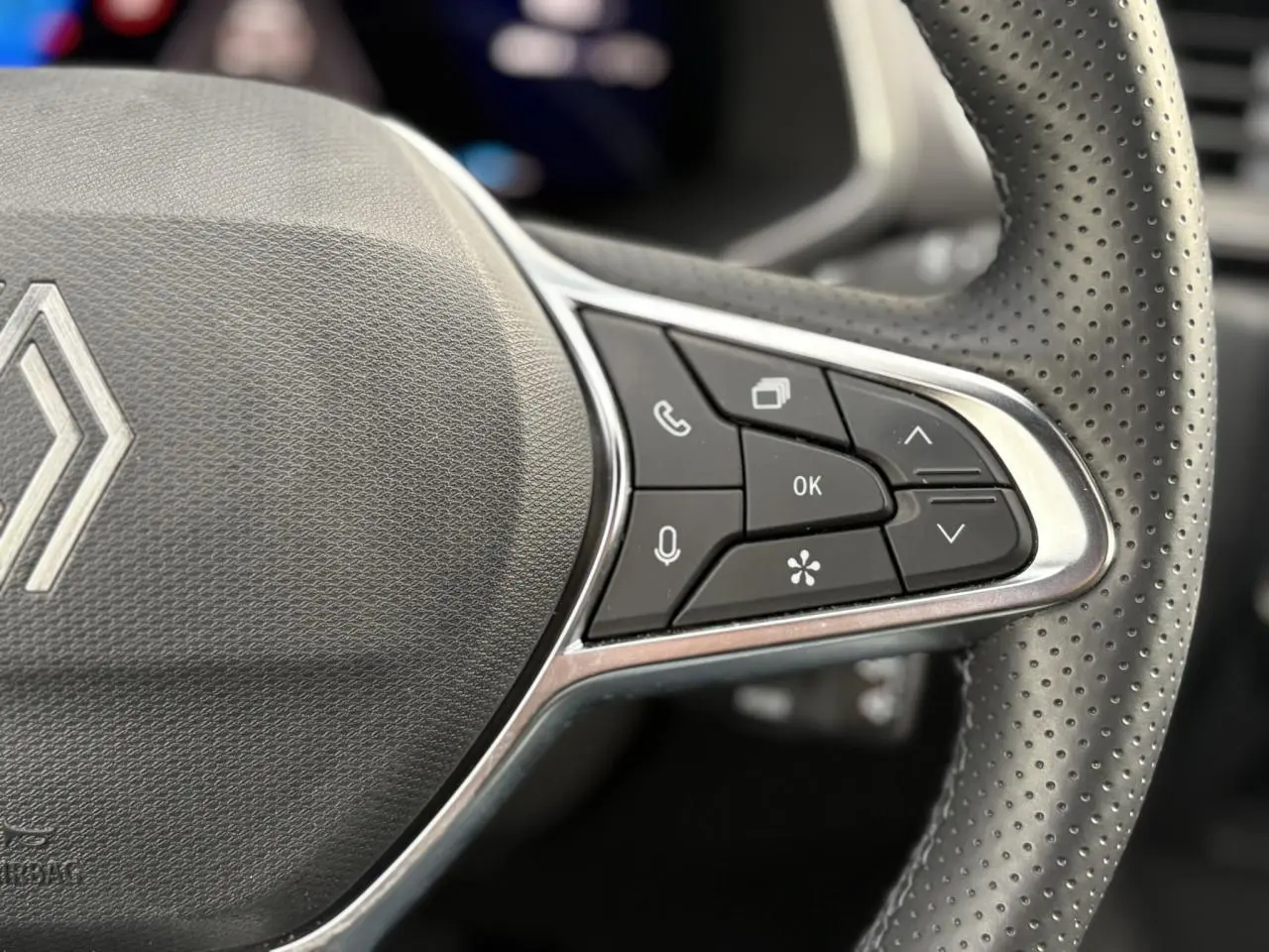 Gros plan sur le côté droit du volant perforé noir de la Renault SYMBIOZ avec commandes multifonctions intégrées.