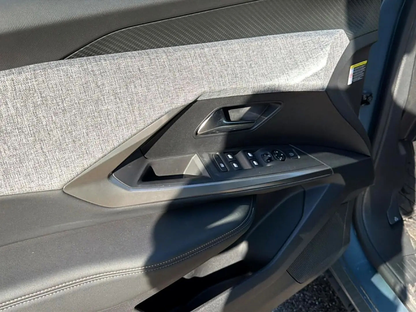 Détail de la porte avant gauche du Peugeot 3008 bleu Ingara, avec commandes des vitres et tissu gris.