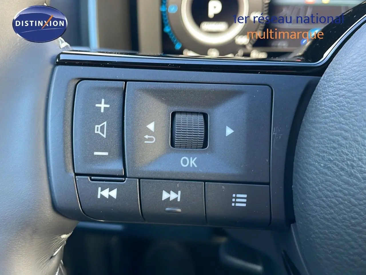 Gros plan sur les commandes au volant du Nissan Qashqai blanc nacré 2025 avec toit noir, affichage digital en arrière-plan.