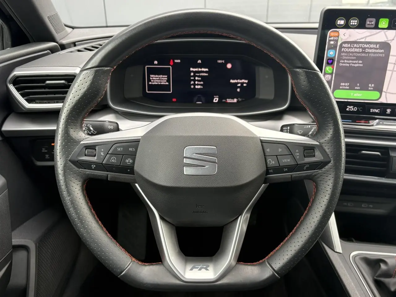Vue rapprochée du volant en cuir perforé noir avec surpiqûres rouges et tableau de bord numérique du SEAT Leon 2025.