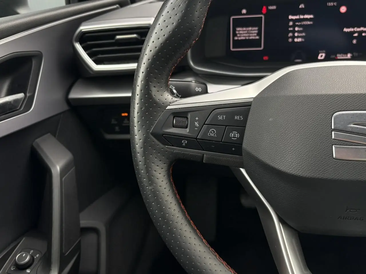 Gros plan sur le volant en cuir perforé avec surpiqûres rouges et commandes multifonctions du SEAT Leon 2025 côté conducteur.