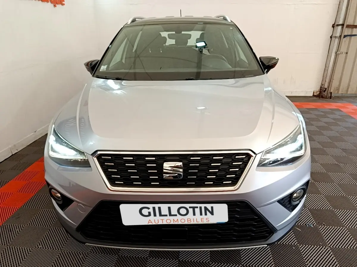 Vue avant d'un SEAT Arona gris clair 2019 avec feux LED allumés dans un showroom.