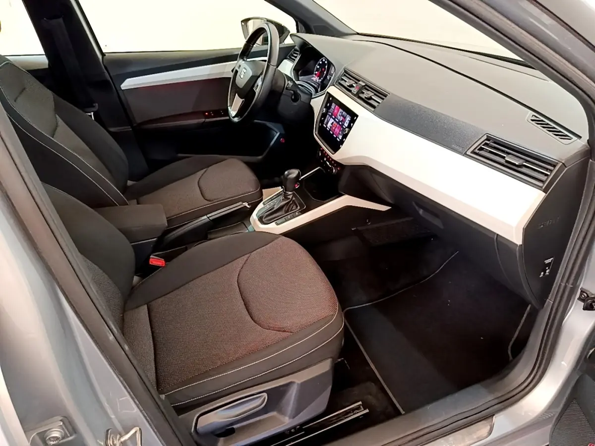 Vue intérieure côté conducteur du SEAT Arona gris clair, mettant en valeur le tableau de bord moderne et les sièges tissus noirs.