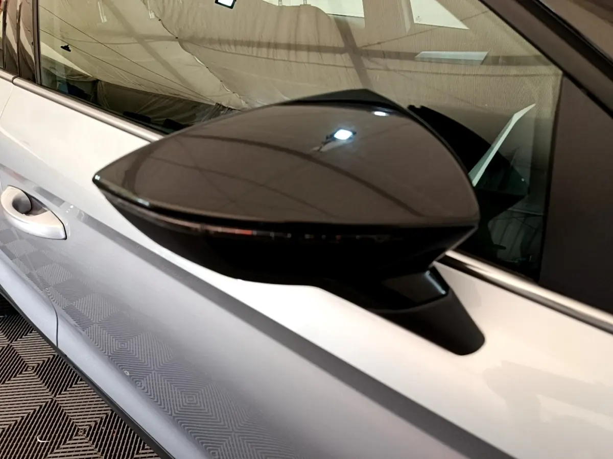 Rétroviseur noir en gros plan sur le côté gauche d’une SEAT Arona gris clair, avec poignée de porte visible.