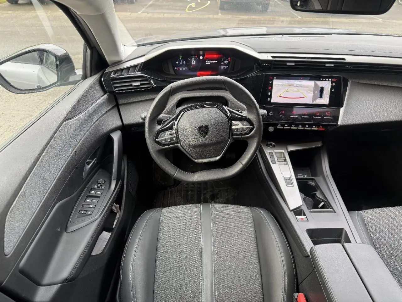 Vue intérieure centrée sur le poste de conduite de la Peugeot 308 gris sellenium, avec volant compact et écran tactile.