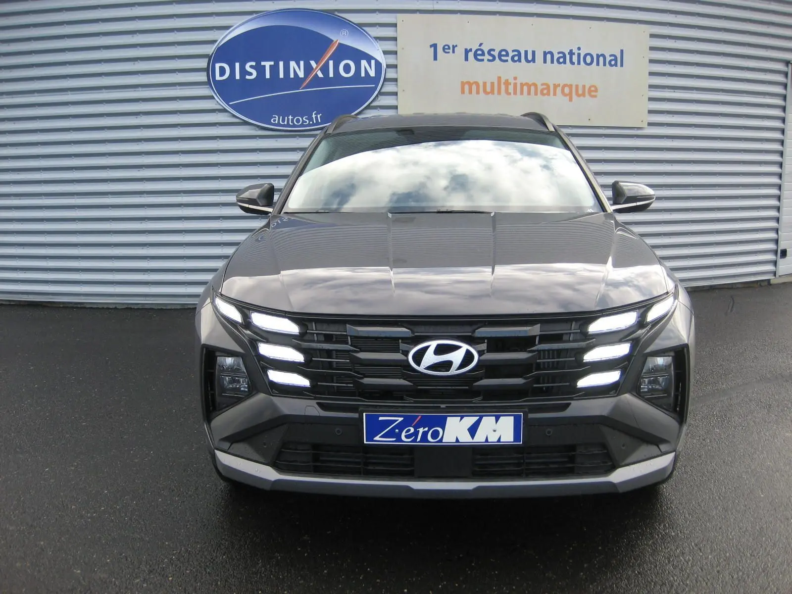 Vue frontale d'un Hyundai Tucson 2025 gris Ecotronic avec feux LED allumés sur un parking extérieur.