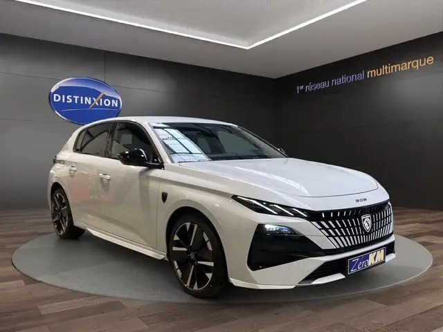 Vue 3/4 avant droite de la Peugeot 308 blanche Okenite, hybride, avec calandre distinctive et jantes noires bicolores.