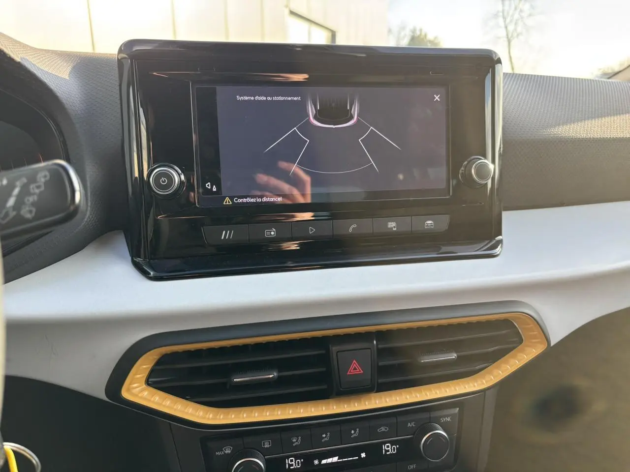 Vue rapprochée de l'écran tactile central affichant l'aide au stationnement dans l'habitacle clair du SEAT Arona blanc.