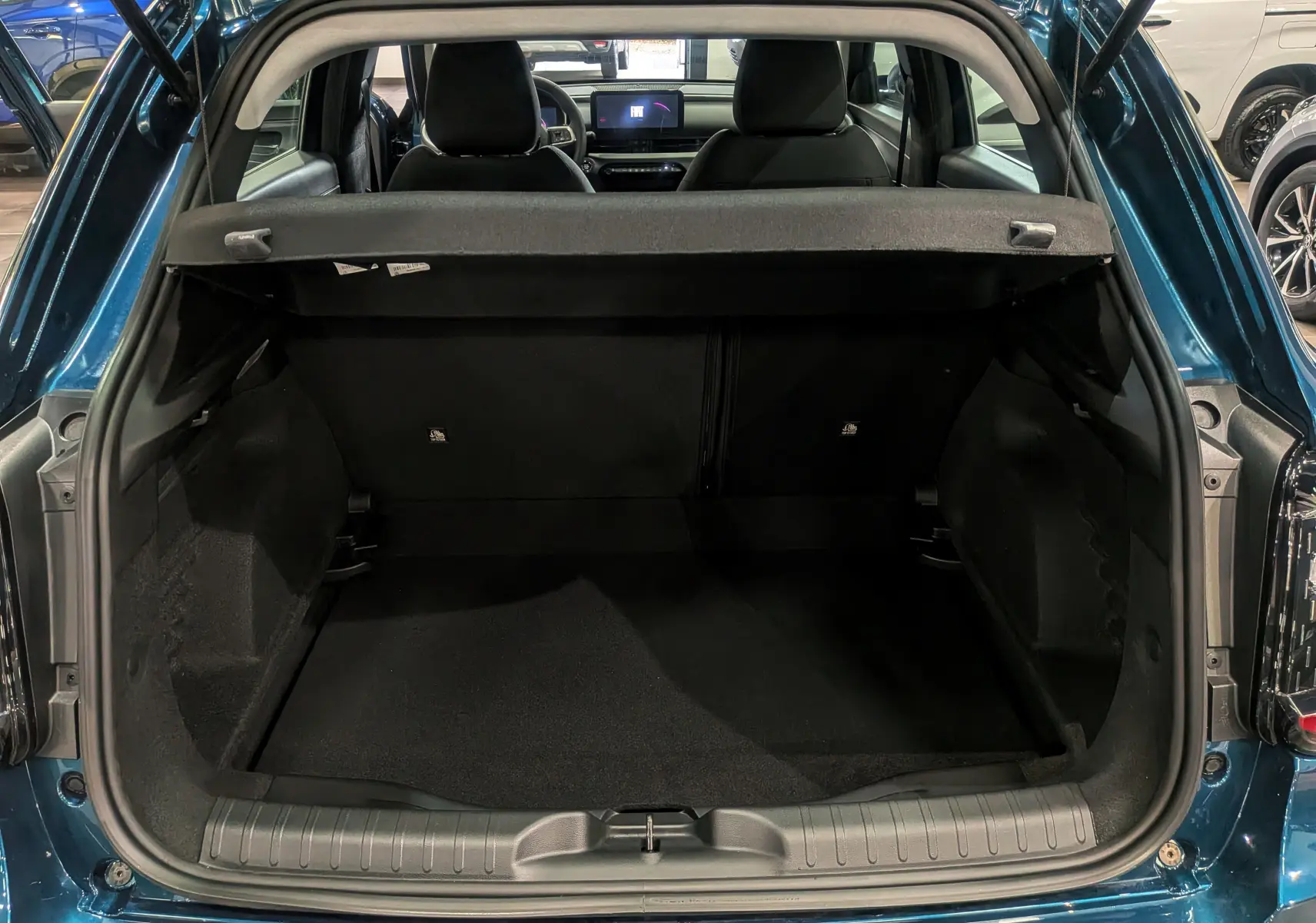 Coffre ouvert vu de l'arrière d'une FIAT 600 1.2 Hybrid bleu Sea, intérieur noir et sièges avant visibles.