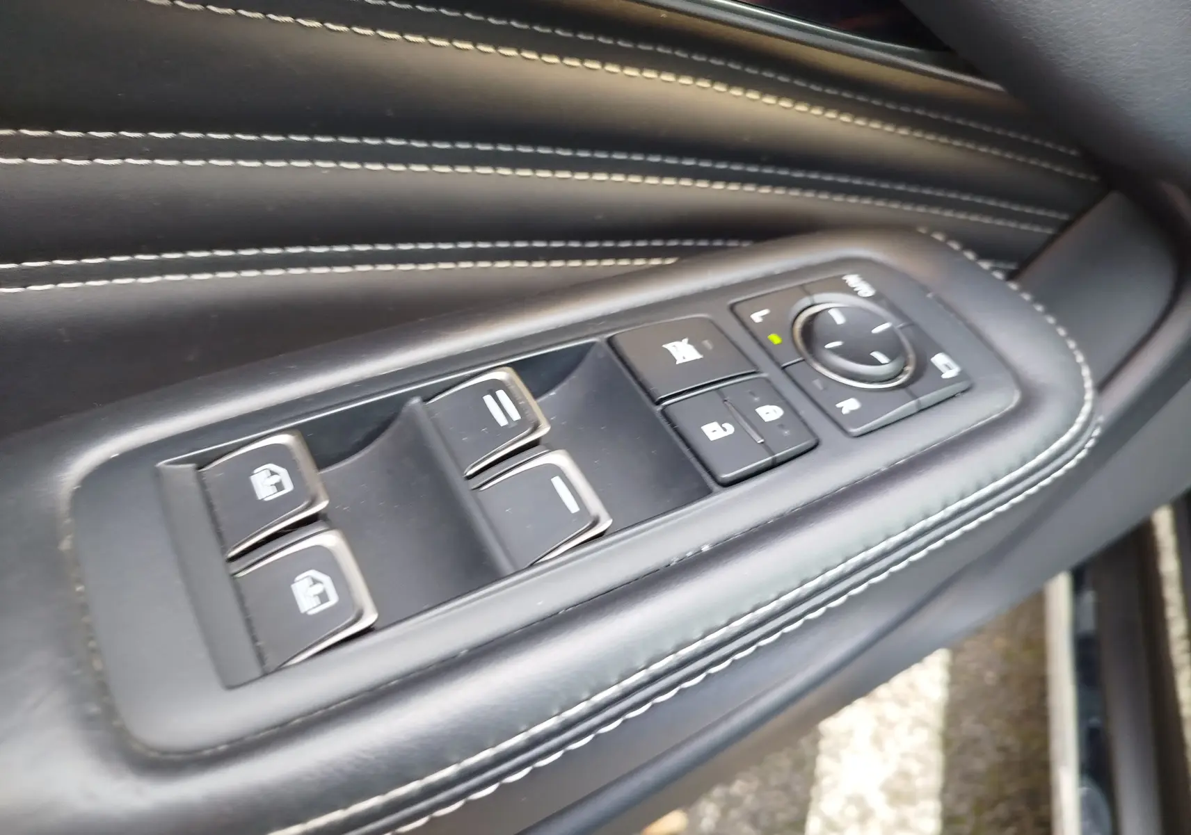 Gros plan sur les commandes de vitres et rétroviseurs sur la porte en cuir noir avec surpiqûres blanches d'une Lexus LS 500H.
