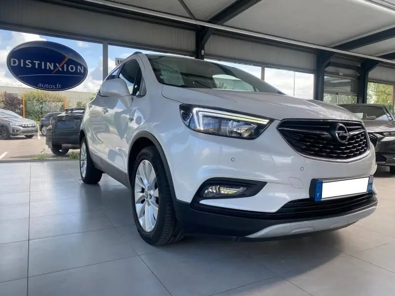 Vue 3/4 avant d'un Opel Mokka blanc 2017 en showroom, avec calandre noire et jantes alliage visibles.