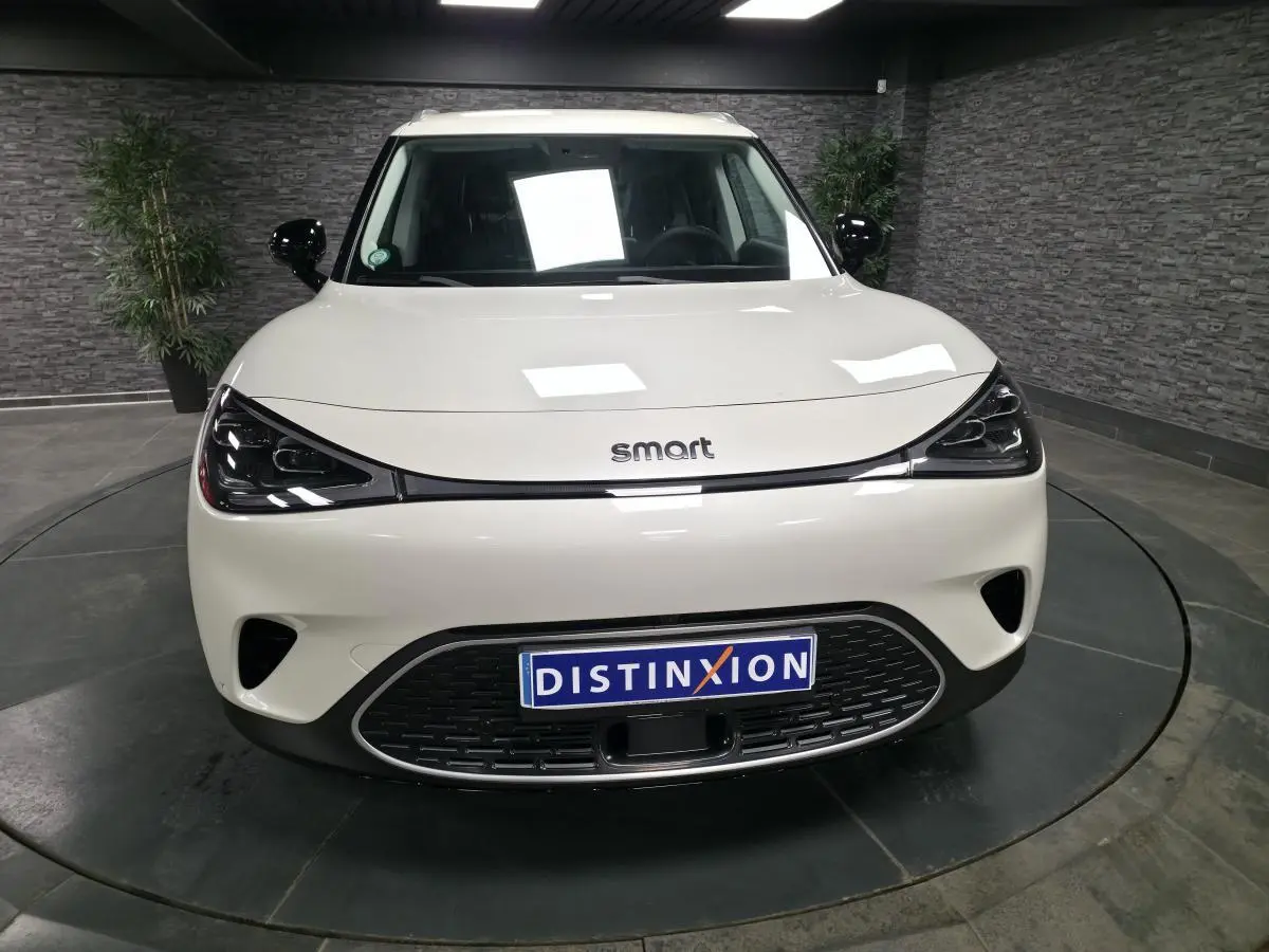 Vue frontale d'une Smart #1 blanche électrique 2024 avec phares LED et calandre noire distinctive.