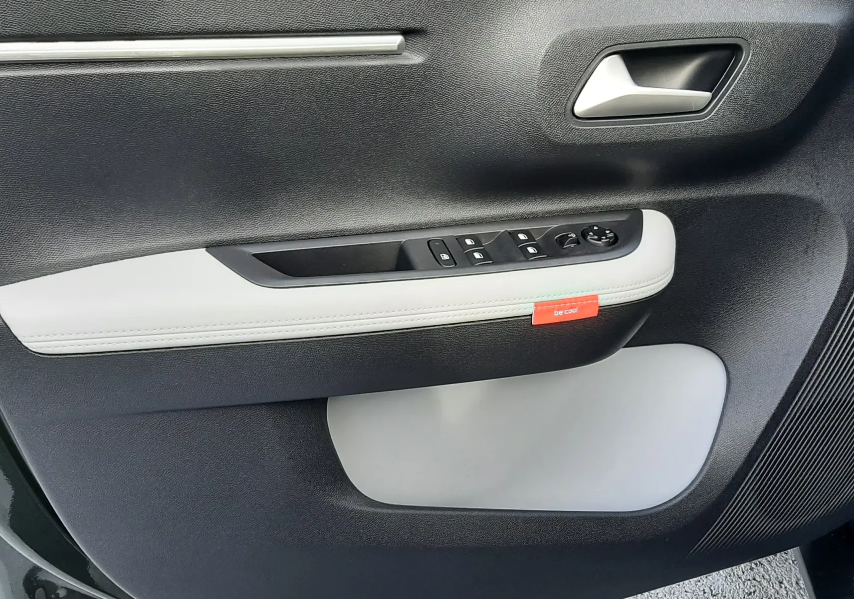 Intérieur de la porte côté conducteur du Citroën C3 Aircross hybride 2026, avec garniture noire et blanche et étiquette rouge "be cool".