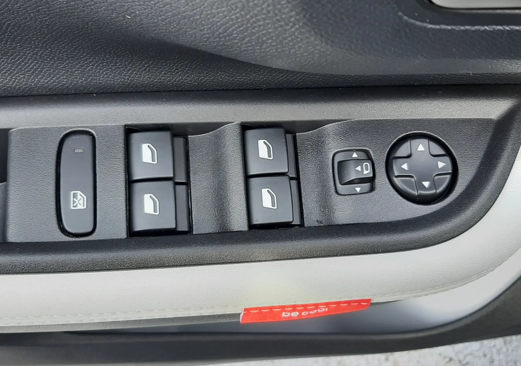 Gros plan sur les commandes de lève-vitres et réglages des rétroviseurs côté conducteur du Citroën C3 Aircross hybride 2026, garniture claire.