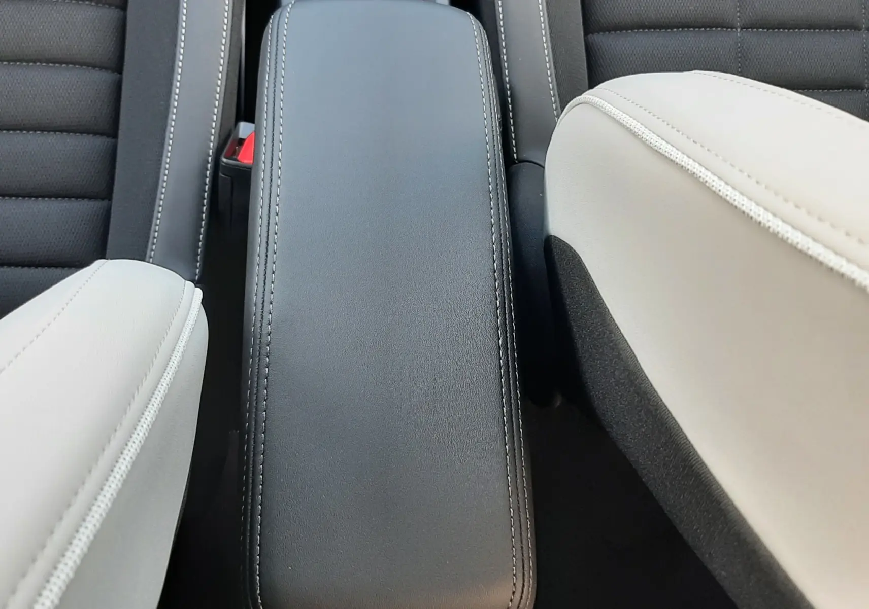 Vue plongeante sur l'accoudoir central noir entre les sièges avant bicolores noir et beige du Citroën C3 Aircross hybride 2026.