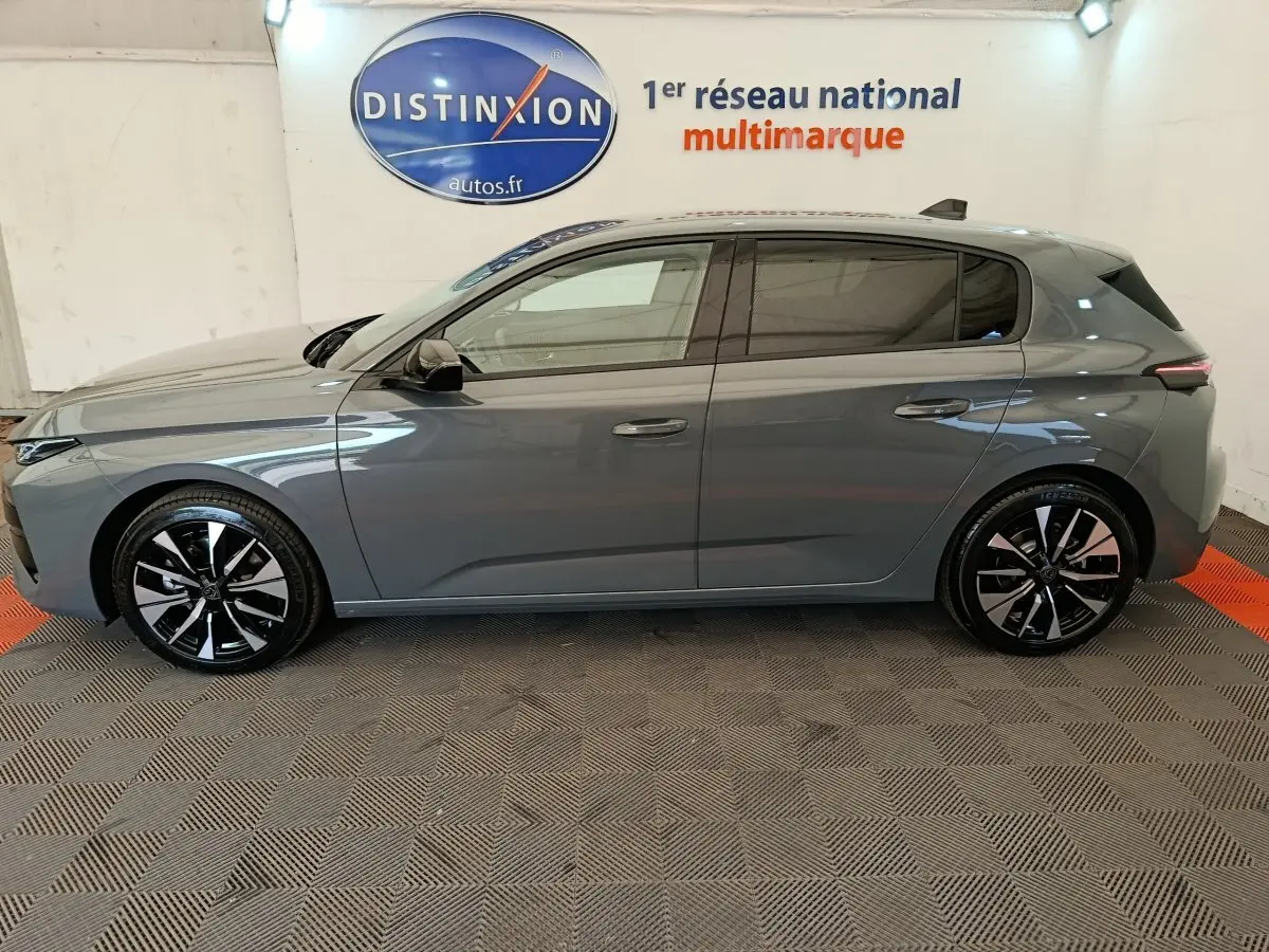 Profil côté gauche d'une Peugeot 308 gris foncé 2026 avec jantes noires et logo Distinxion en arrière-plan.