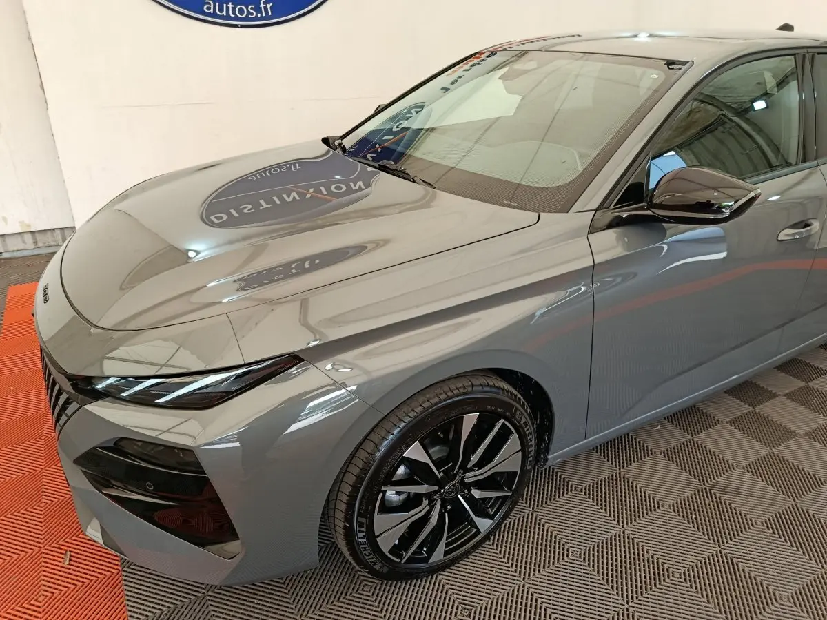 Vue 3/4 avant droit d'une Peugeot 308 gris foncé 2026 avec jantes noires et phares LED fins.