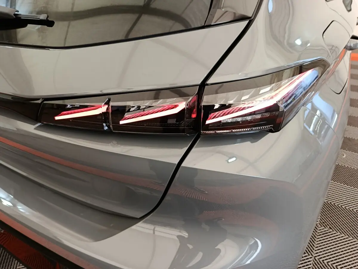 Feu arrière droit allumé sur Peugeot 308 gris foncé, vue rapprochée du coin arrière du véhicule.