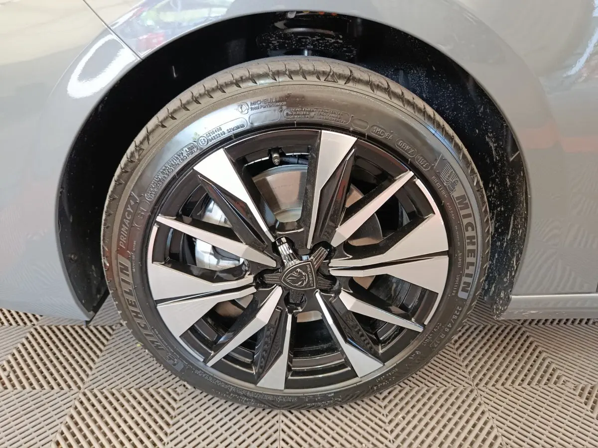 Gros plan sur la roue avant droite d'une Peugeot 308 gris foncé, jante alliage bicolore au design moderne.