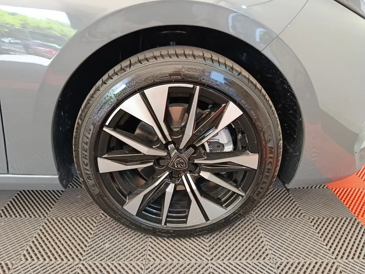 Gros plan sur la roue avant droite d'une Peugeot 308 gris foncé, avec jante alliage noire et argentée au design moderne.