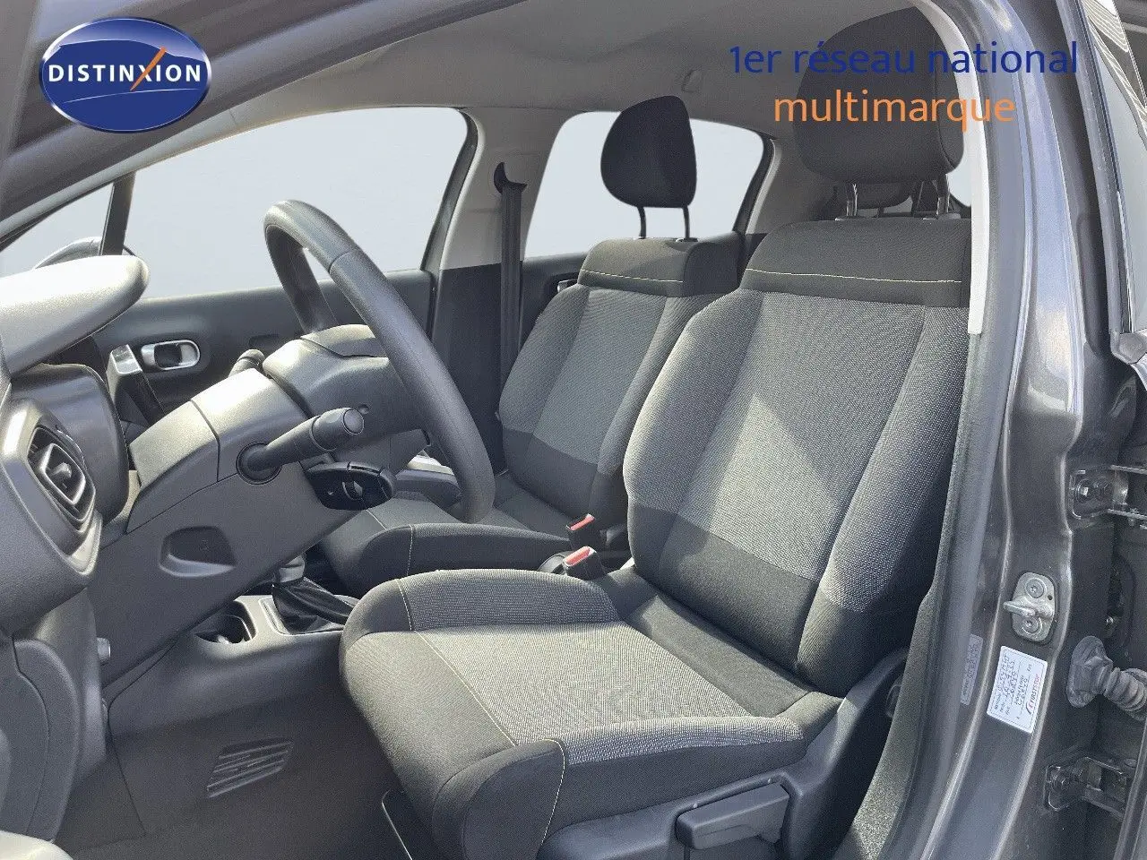 Intérieur avant droit de la Citroën C3 gris platinium métal 2023 avec sièges tissu gris et volant multifonction.