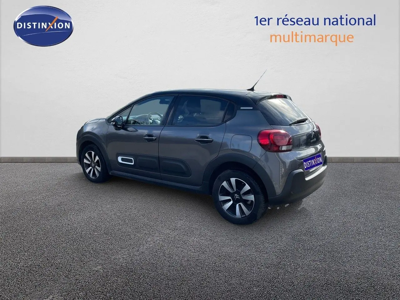 Citroën C3 gris platinium métal vue 3/4 arrière côté gauche avec jantes bi-ton et protections latérales blanches.
