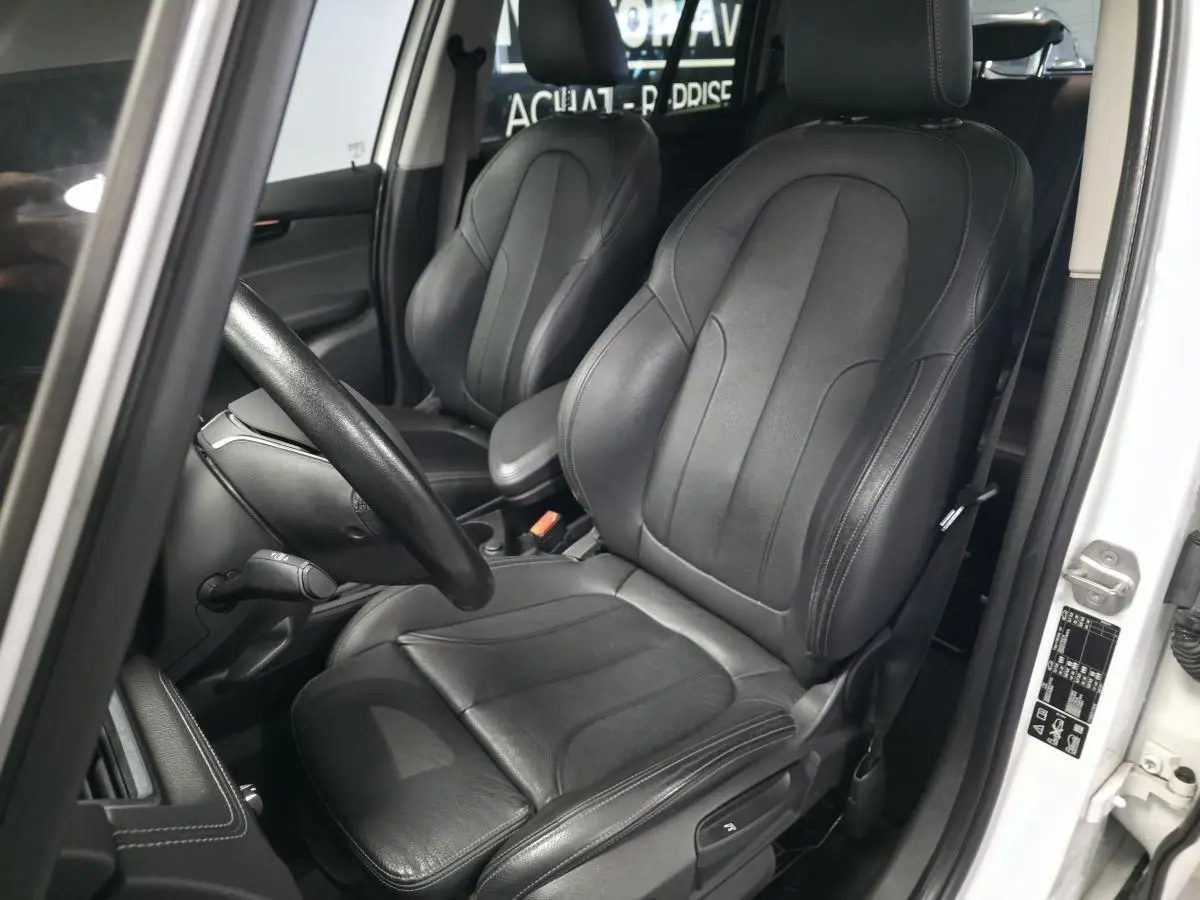 Vue intérieure côté conducteur de la BMW Série 2 Gran Tourer 218d xDrive blanche avec sièges cuir noirs et volant sport.