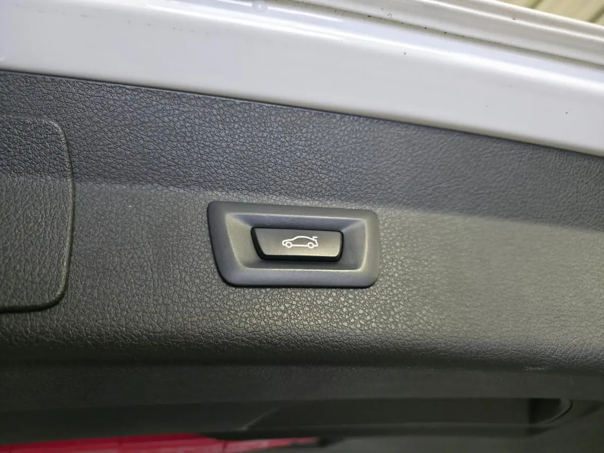 Bouton d'ouverture électrique du hayon sur le bord intérieur du coffre d'une BMW Série 2 blanc.