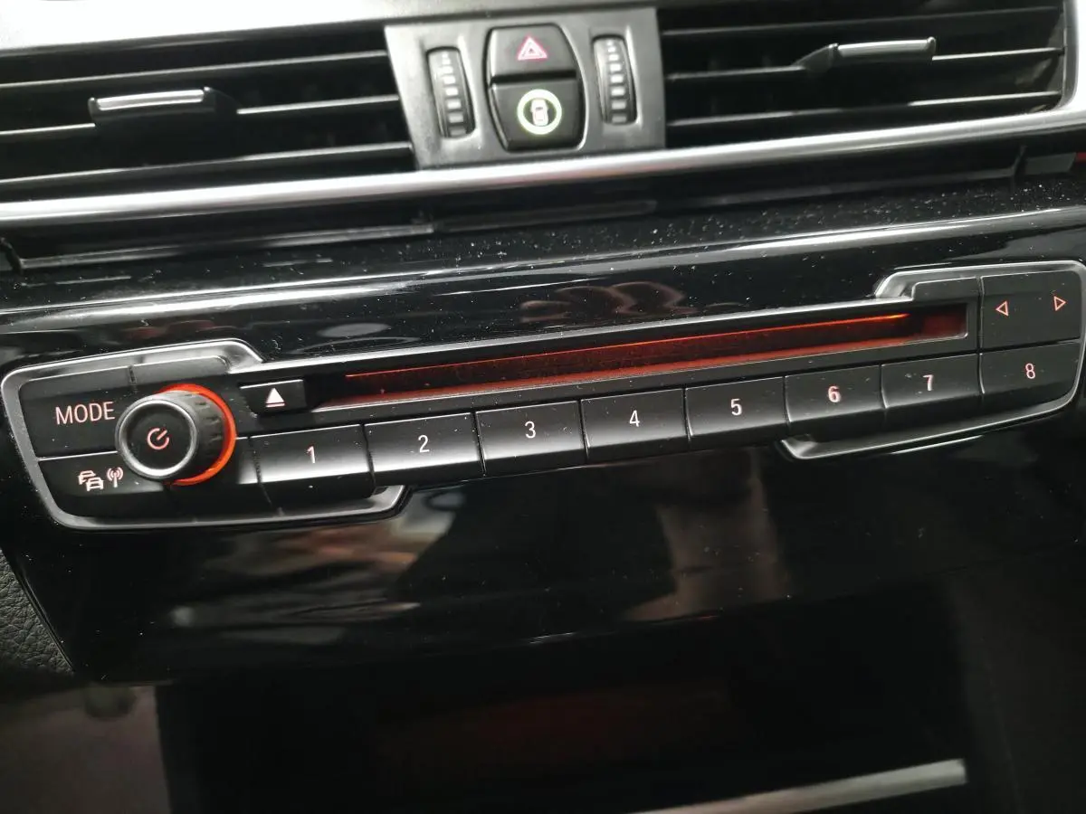 Gros plan sur la commande radio noire avec boutons numérotés et molette rouge dans l'habitacle d'une BMW Série 2 Gran Tourer blanche.