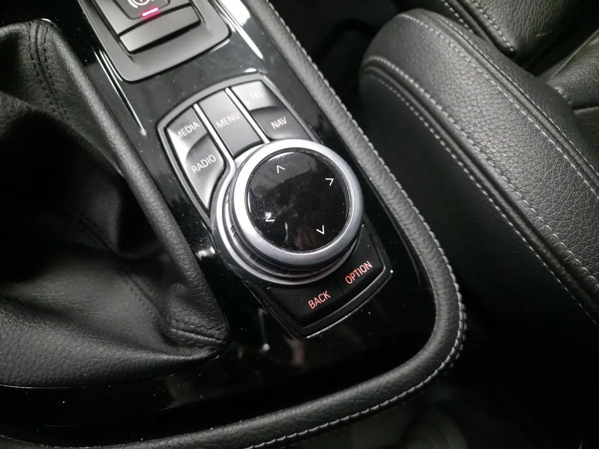 Gros plan sur la molette de commande iDrive noire et argentée, entourée de cuir noir sur la console centrale d'une BMW Série 2 Gran Tourer.
