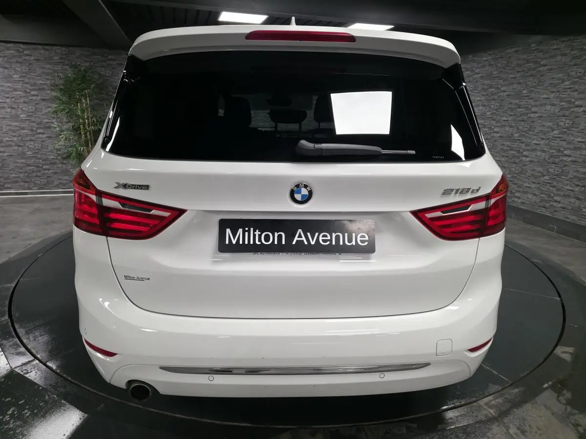 Vue arrière d'une BMW Série 2 Gran Tourer blanche avec badges xDrive et 218d dans un showroom.