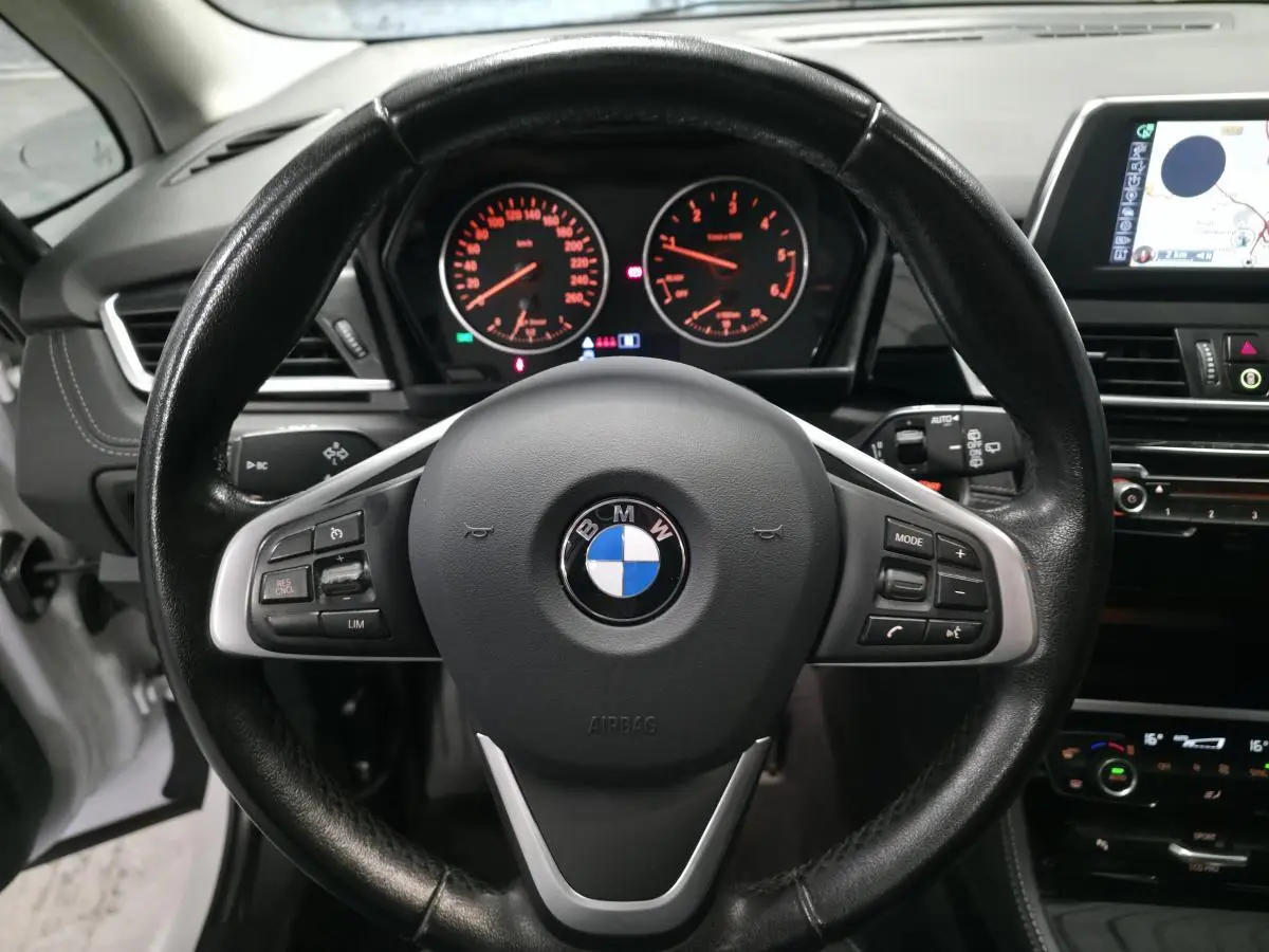 Vue rapprochée du volant cuir noir et du tableau de bord éclairé d'une BMW Série 2 Gran Tourer blanche de 2016.