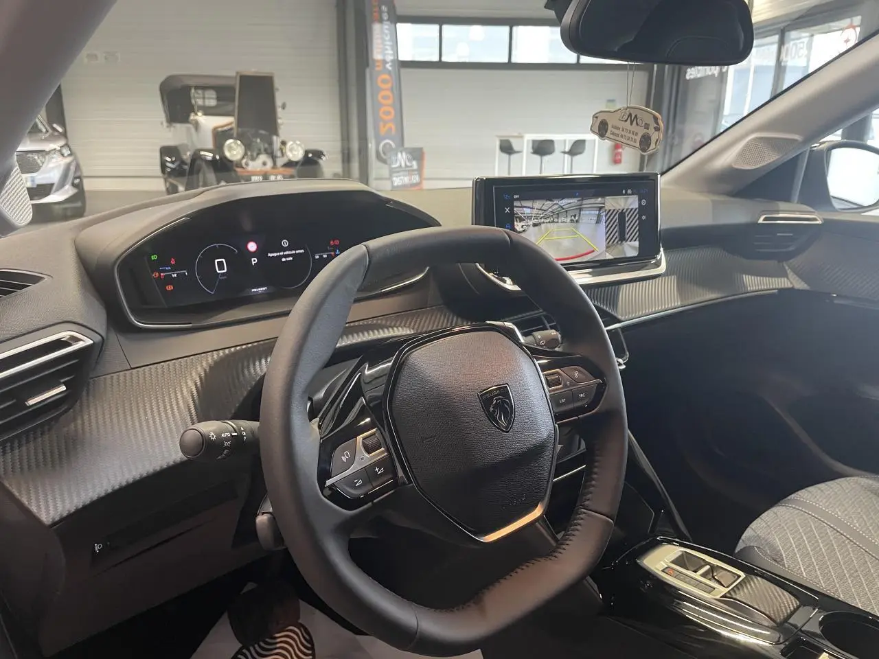 Intérieur Peugeot 208 2025 vu côté conducteur, volant compact cuir et écran tactile avec caméra de recul.