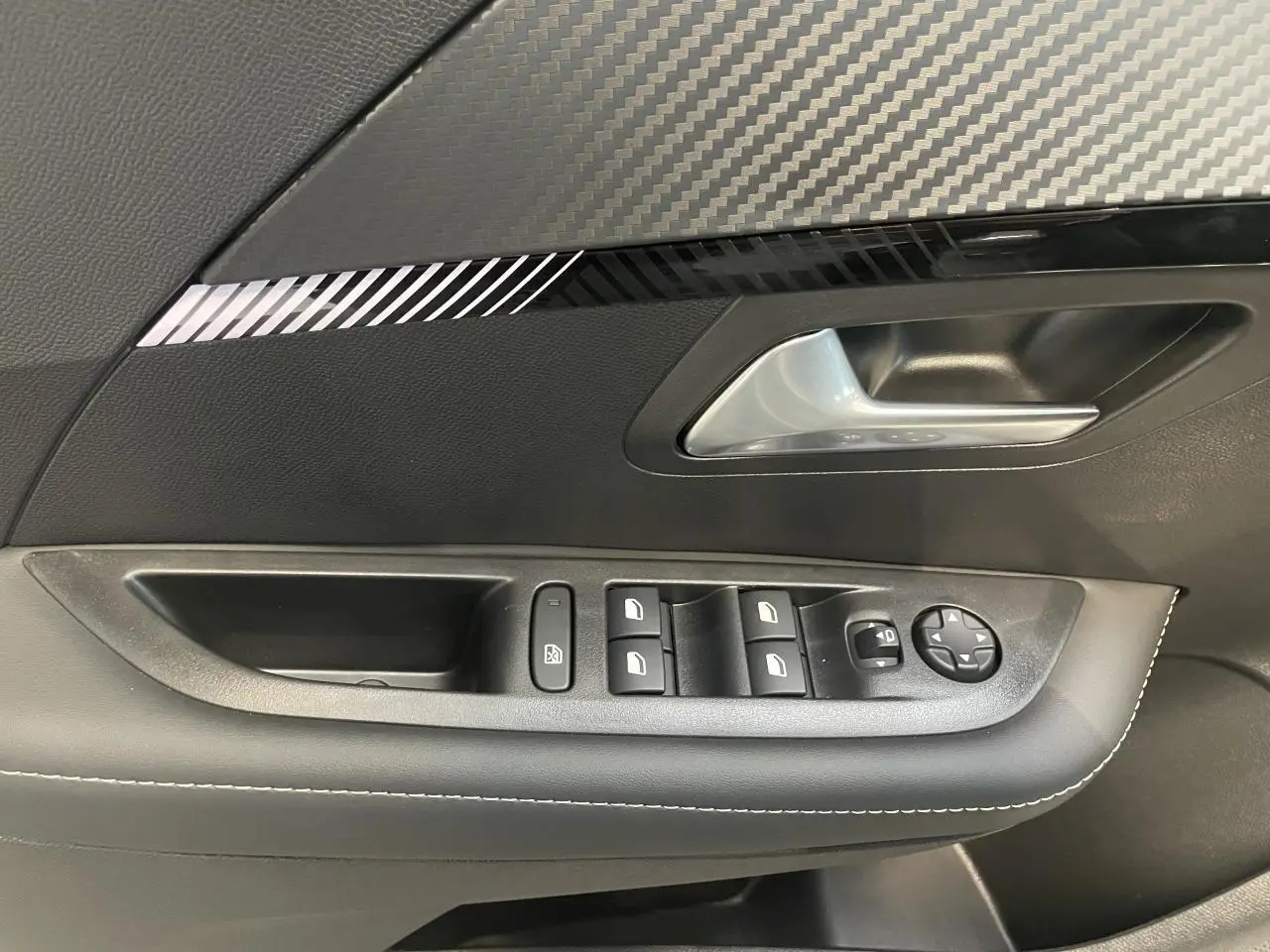 Poignée de porte intérieure côté gauche avec commandes de vitres et décor carbone sur Peugeot 208 Gris Artense 2025.