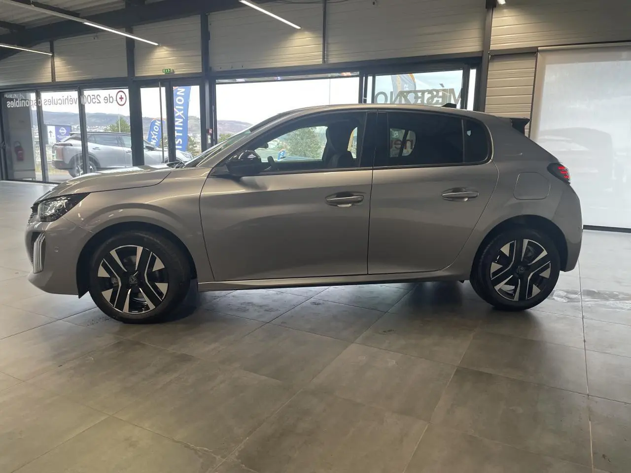 Peugeot 208 gris Artense vue de profil côté gauche en intérieur avec jantes alliage bi-ton.