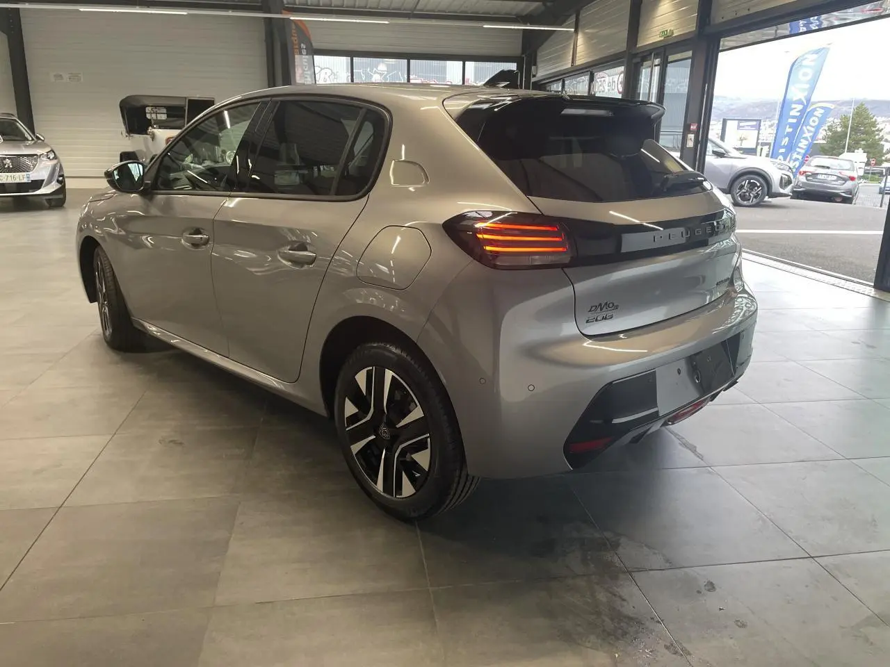 Peugeot 208 gris Artense vue 3/4 arrière droit en intérieur, feux arrière LED et jantes alliage bi-ton visibles