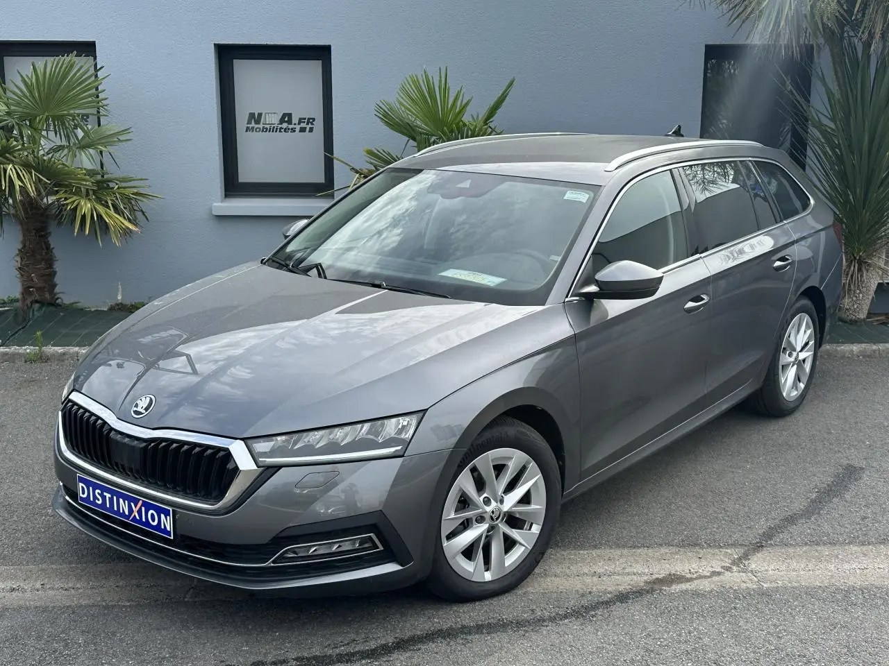 Vue 3/4 avant droite d'une Skoda Octavia Combi gris graphite avec calandre chromée et barres de toit argentées.