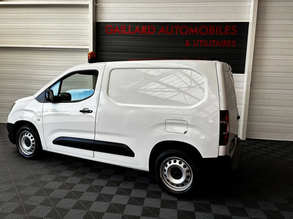 Vue de profil côté gauche d'un utilitaire Opel Combo blanc avec cloison pleine et jantes acier en intérieur showroom.