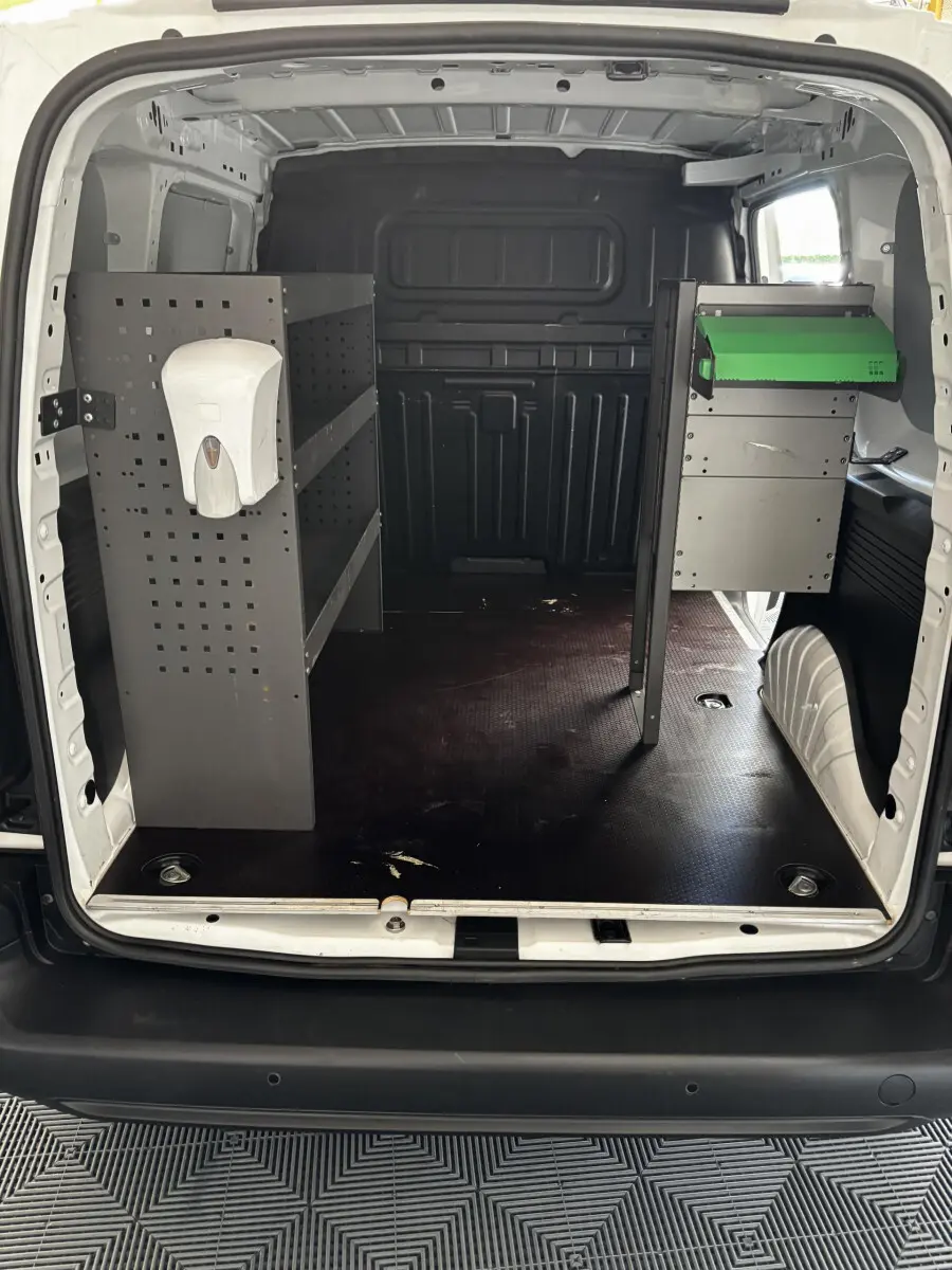 Vue arrière ouverte du fourgon blanc Opel Combo 1.5 diesel, montrant l'aménagement intérieur avec étagères métalliques et distributeur de gel.