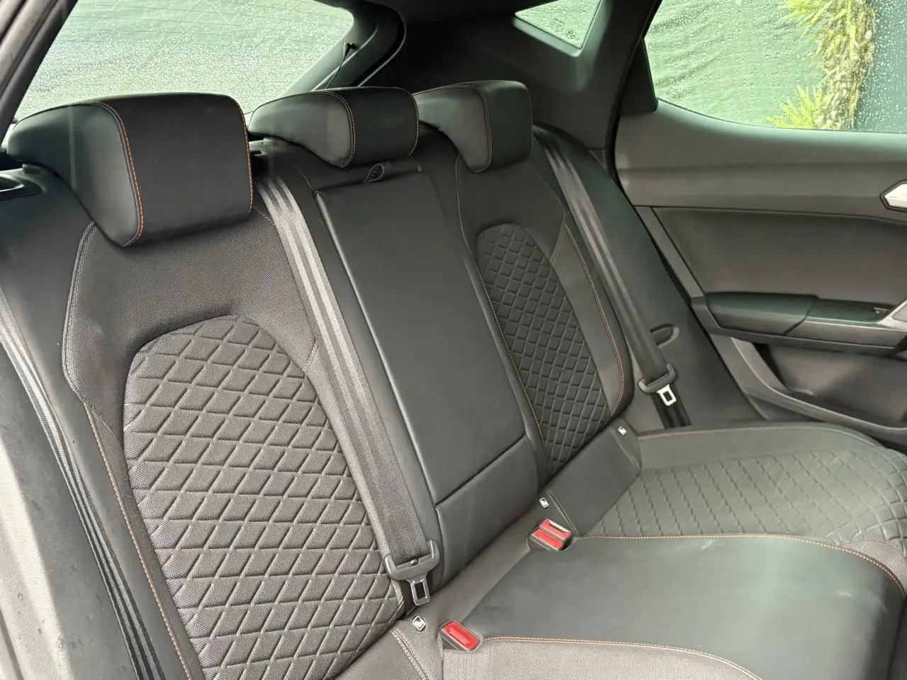 Vue latérale des sièges arrière noirs avec surpiqûres rouges du SEAT LEON 2024, finition FR, intérieur élégant.