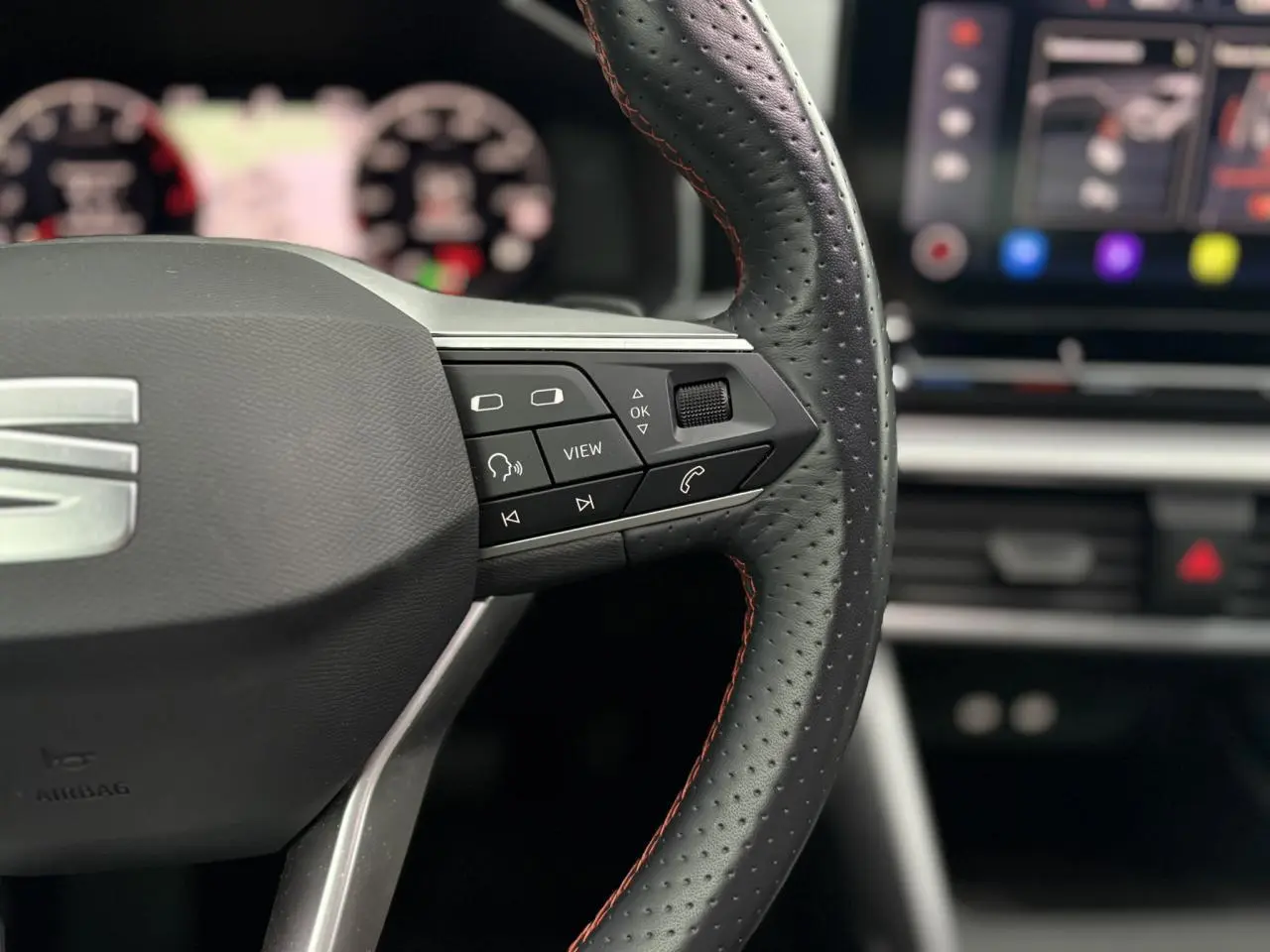 Gros plan sur le volant cuir perforé avec surpiqûres rouges du SEAT LEON 2024, boutons multifonctions visibles côté droit.