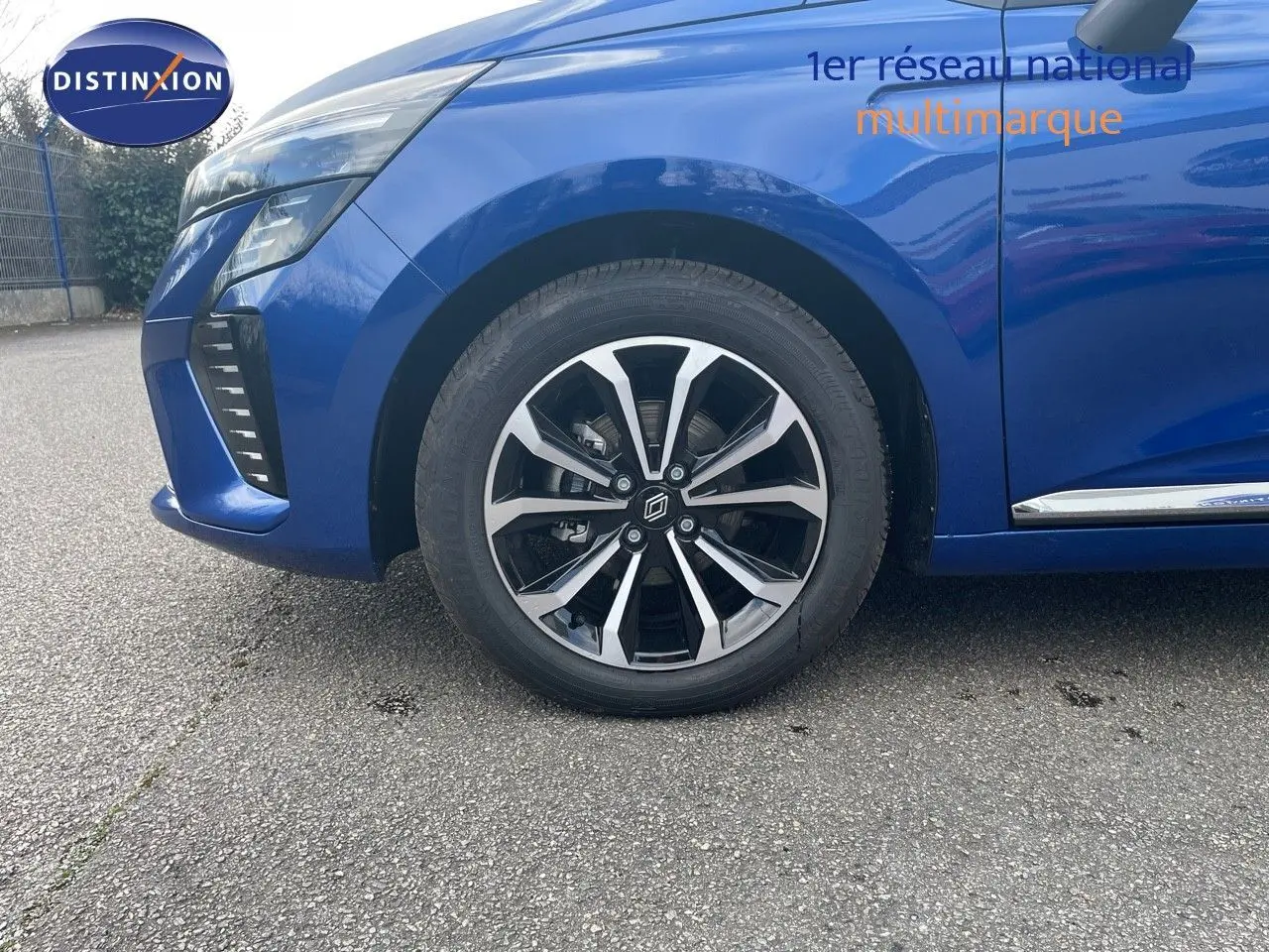 Gros plan sur la roue avant gauche et l'aile d'une Renault Clio TCE 90CH TECHNO bleu iron metal, avec jante alliage bicolore.