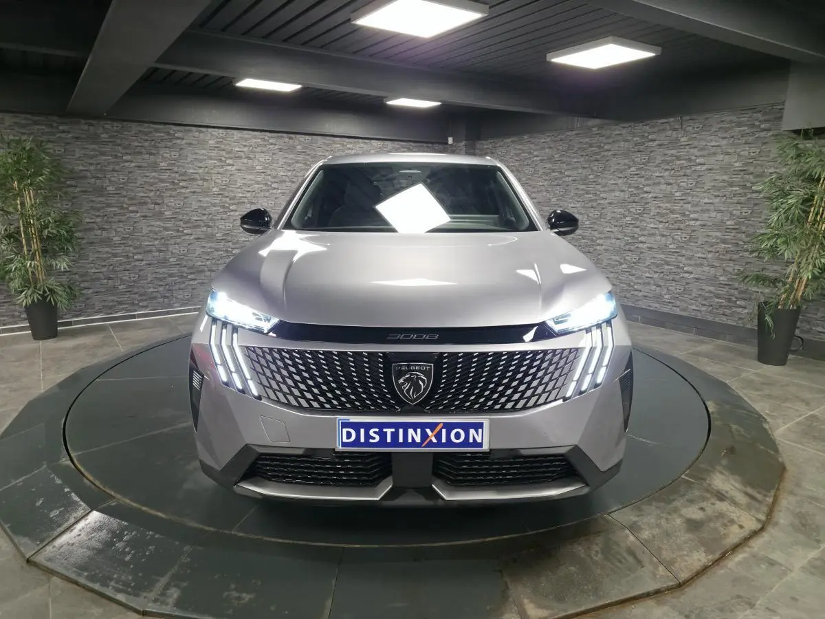 Vue frontale d'un Peugeot 3008 gris métallisé avec calandre noire laquée et feux LED allumés dans un showroom.