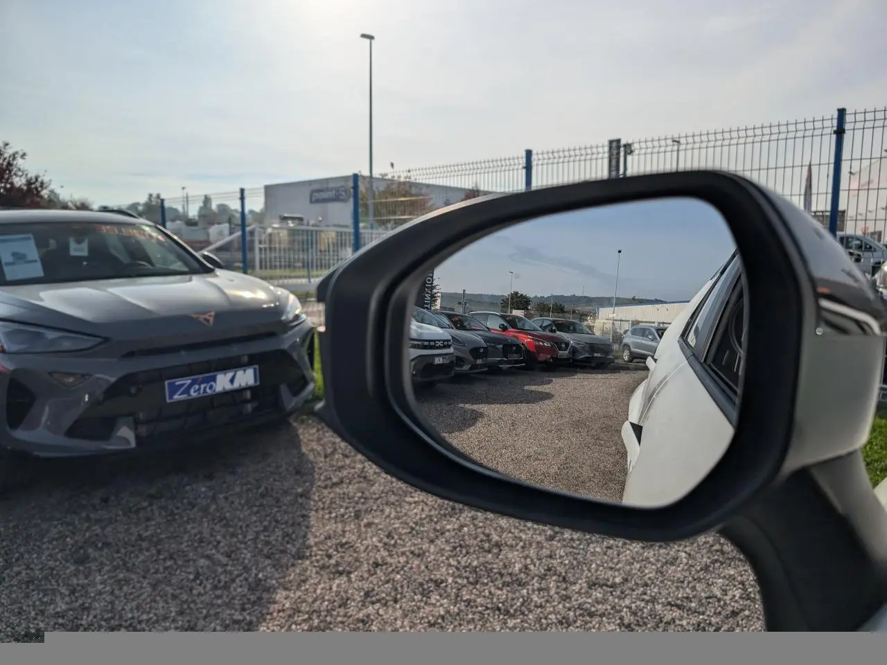 Rétroviseur droit montrant la carrosserie blanche du Toyota C-HR 2024 en partie, avec vue sur un parking de voitures.