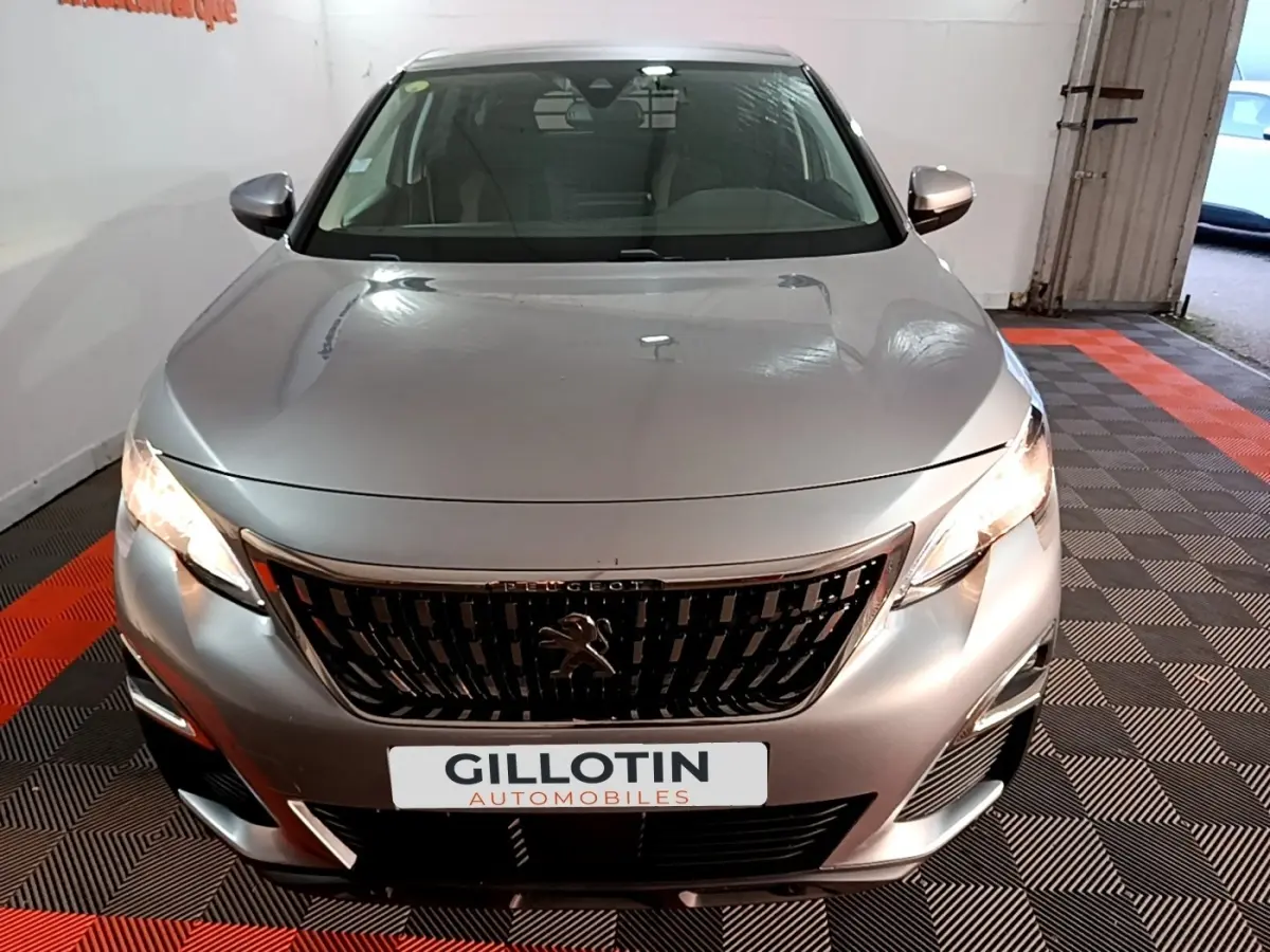 Vue avant d'un Peugeot 5008 gris clair 2020 avec calandre noire et phares allumés en intérieur showroom.