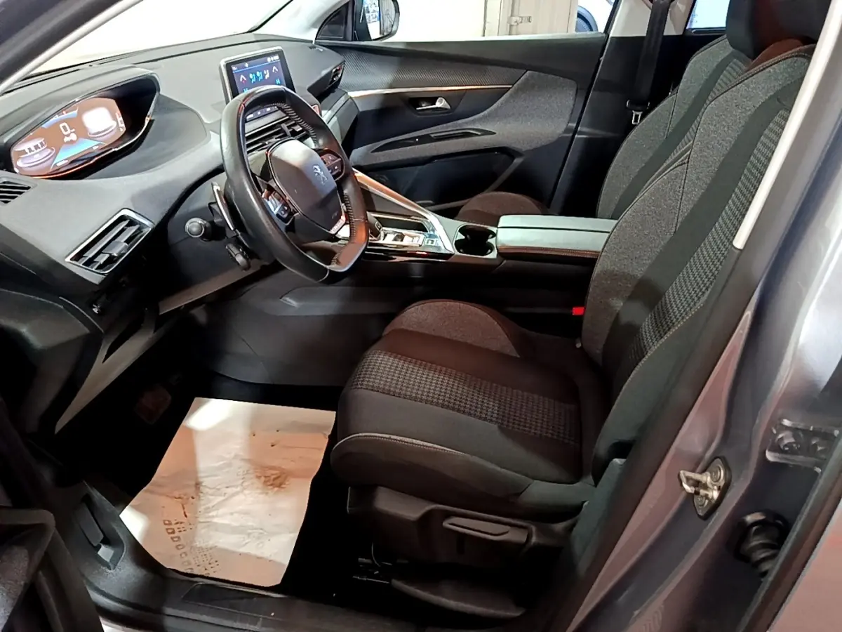 Vue intérieure côté conducteur du Peugeot 5008 gris clair 2020, mettant en valeur le tableau de bord digital et les sièges tissu bicolores.