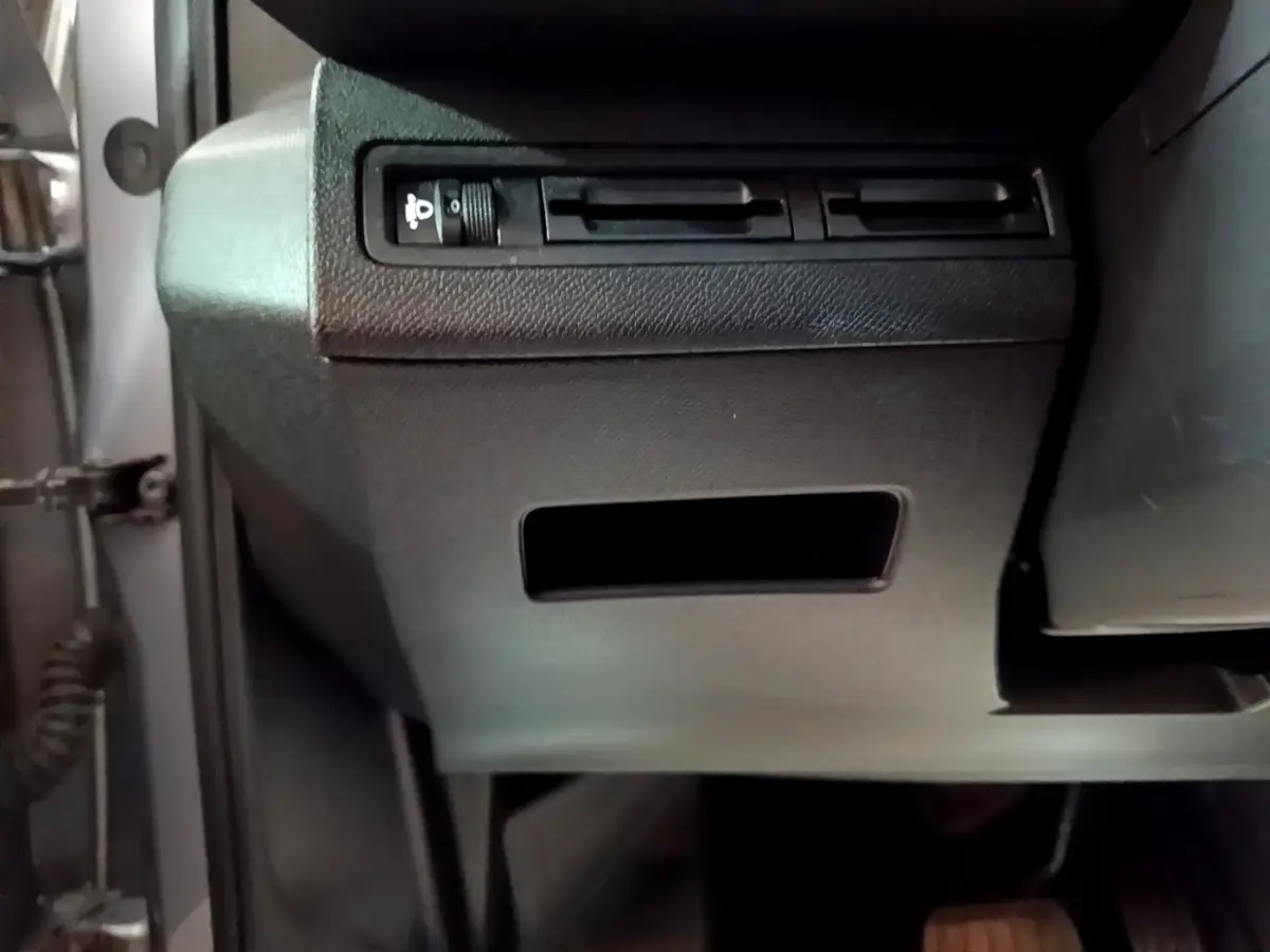 Vue rapprochée sous le tableau de bord côté gauche du Peugeot 5008 gris clair, montrant les commandes d’éclairage.