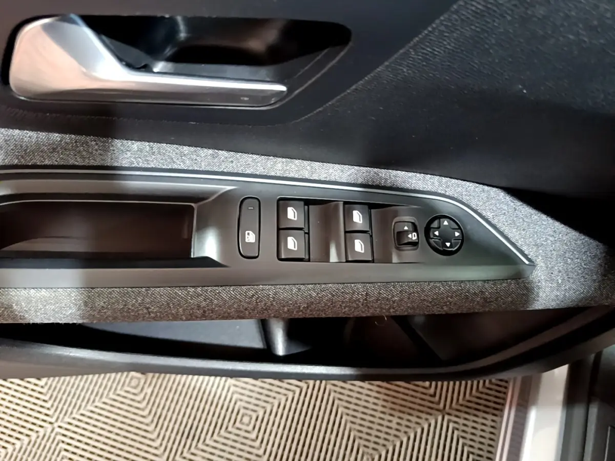 Gros plan sur la commande des vitres et rétroviseurs côté conducteur du Peugeot 5008 gris clair, intérieur tissu gris.