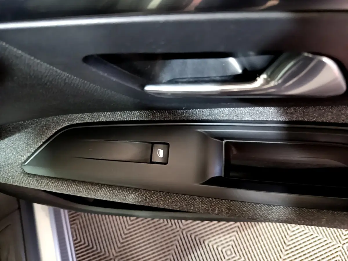 Gros plan sur la poignée intérieure et le bouton de lève-vitre côté conducteur du Peugeot 5008 gris clair 2020.