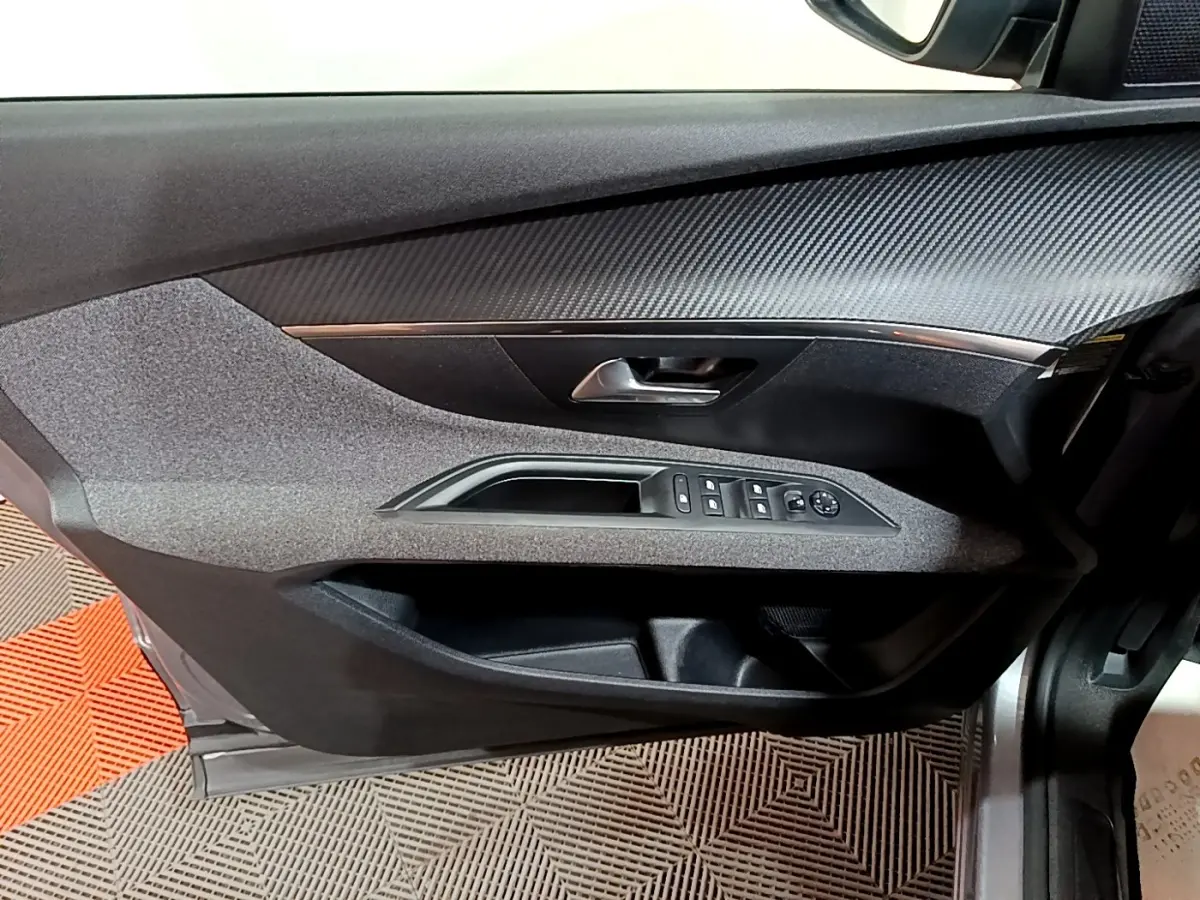 Vue rapprochée de la porte avant gauche du Peugeot 5008 gris clair, montrant les commandes des vitres et le revêtement texturé.